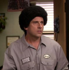 a man with an afro on his head wearing a gray shirt and holding a knife