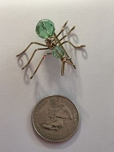 a small green spider brooch sitting on top of a dime coin with tiny branches attached to it