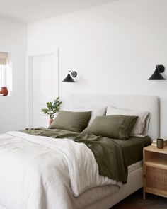 a white bed with green sheets and pillows