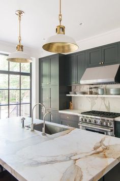 a large kitchen with marble counter tops and black cabinetry, along with two pendant lights