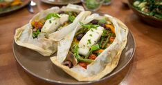 three burritos are sitting on a plate with salad in the background and other dishes