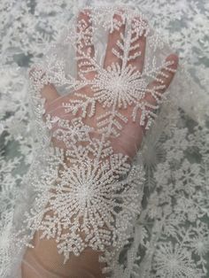 a person's hand is covered with white lace and snowflakes on it