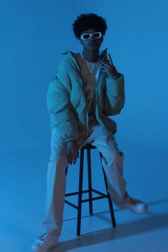 a man sitting on top of a stool with sunglasses on his face and one hand in the air