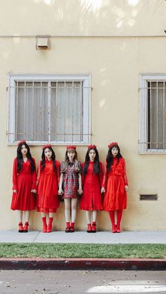 four girls in red dresses standing next to each other on the side of a building