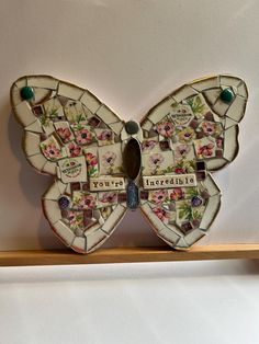 a mosaic butterfly with words and pictures on it's wings, sitting on a shelf