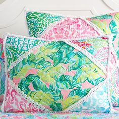 two colorful pillows sitting on top of a bed next to a white headboard and night stand