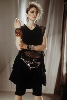 a woman in black dress and bracelets holding her hand up to the side with both hands