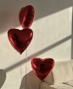 two red heart shaped balloons floating in the air next to a white couch with pillows