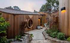 a wooden building with a circular mirror on it's wall next to a garden