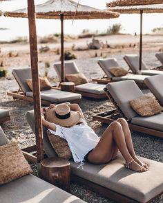 a woman laying on top of a beach next to lounge chairs and an umbrella over her head