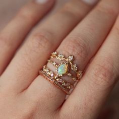 a woman's hand wearing a gold ring with an opal and diamond center