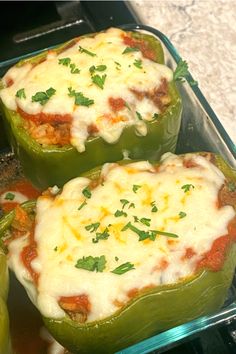 two green peppers with cheese and sauce in a glass dish on a stove top, ready to be cooked