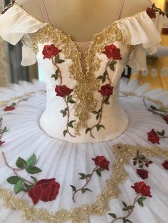 a white and gold dress with red roses on the bottom is displayed in front of a mannequin