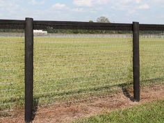 a black wire fence in the middle of a grassy field with a white truck behind it