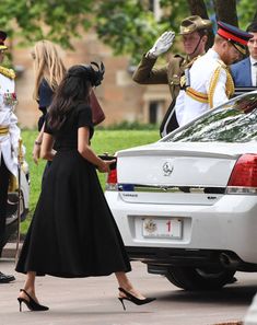 a woman in a black dress is standing next to a white car and some soldiers