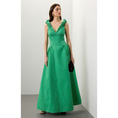 a woman in a green dress stands against a white wall