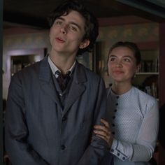 two people standing next to each other in front of a book shelf with books on it