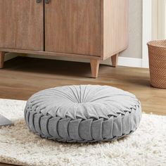 a round floor pillow sitting on top of a white rug next to a wooden cabinet