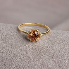 an orange diamond ring sitting on top of a gray cloth covered surface with a white background