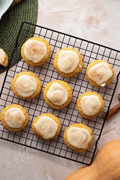 several cookies with icing on a cooling rack next to pumpkins and cinnamon sticks