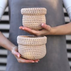 two crocheted baskets being held in front of a woman's face with her hands