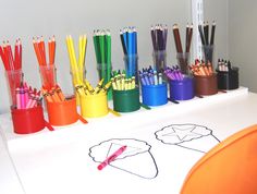 there are many different colored pencils on the table with markers and pens in them