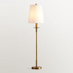 a floor lamp with a white shade on it's side and a gold base