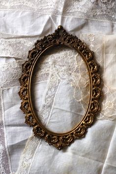 an oval gold frame sitting on top of a white lace covered tablecloth with lacy doily