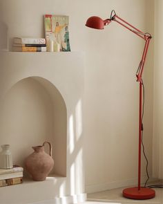 a red floor lamp sitting on top of a white shelf next to a pink vase