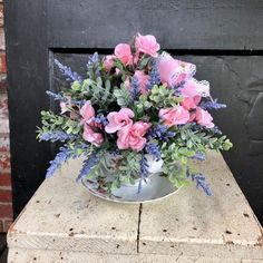 a metal bowl filled with pink flowers sitting on top of a wooden table next to a black door