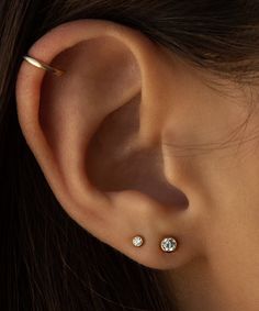 a woman's ear with two small diamond studs