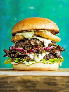 a hamburger with meat, lettuce and onions on a wooden table next to a blue wall