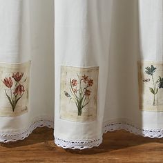 two embroidered curtains with flowers on them are shown in front of a wooden floor and wall