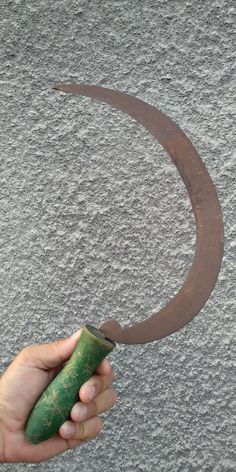 a hand holding a green object in front of a circle on the ground with sand