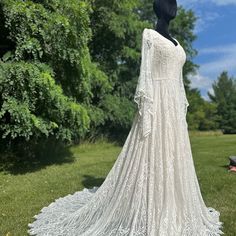 a white wedding dress on display in the grass with trees and blue sky behind it