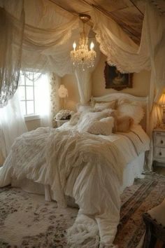 a white bed sitting under a chandelier in a bedroom next to a window