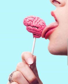 a woman holding a lollipop with a pink brain on it's stick