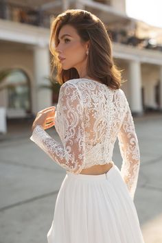 a woman wearing a white wedding dress with long sleeves and lace detailing on the back