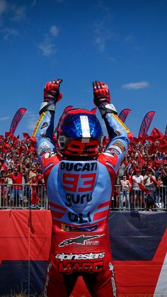 a motorcyclist with his hands up in the air at a race track