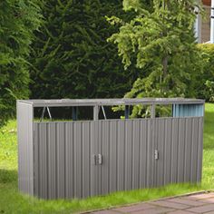 a metal storage shed sitting on top of a brick walkway next to a lush green forest