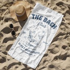 a towel that is laying in the sand next to some sunglasses and a straw hat