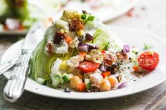 a white plate topped with lettuce, tomatoes and chickpeas next to a fork