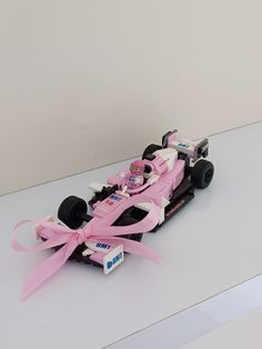 a pink toy race car with ribbon tied around it's front wheel on a white surface