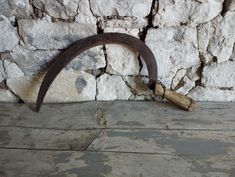 an old rusted metal hook on the side of a stone wall next to a hammer