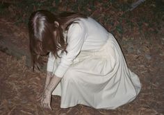 a woman kneeling down on the ground with her hands in her pockets while wearing a white dress