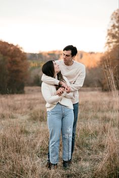 a man and woman standing in the middle of a field with their arms around each other