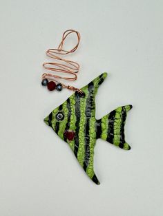 a green and black striped fish ornament on a white surface with copper wire