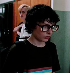 a young boy wearing glasses standing in front of a refrigerator