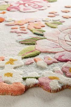 a white rug with pink, yellow and green flowers on it's edges is laying on the floor