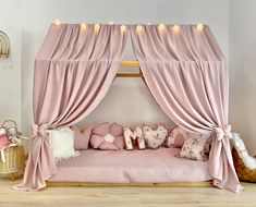 a pink canopy bed with pillows and lights on the top, in a girls'bedroom